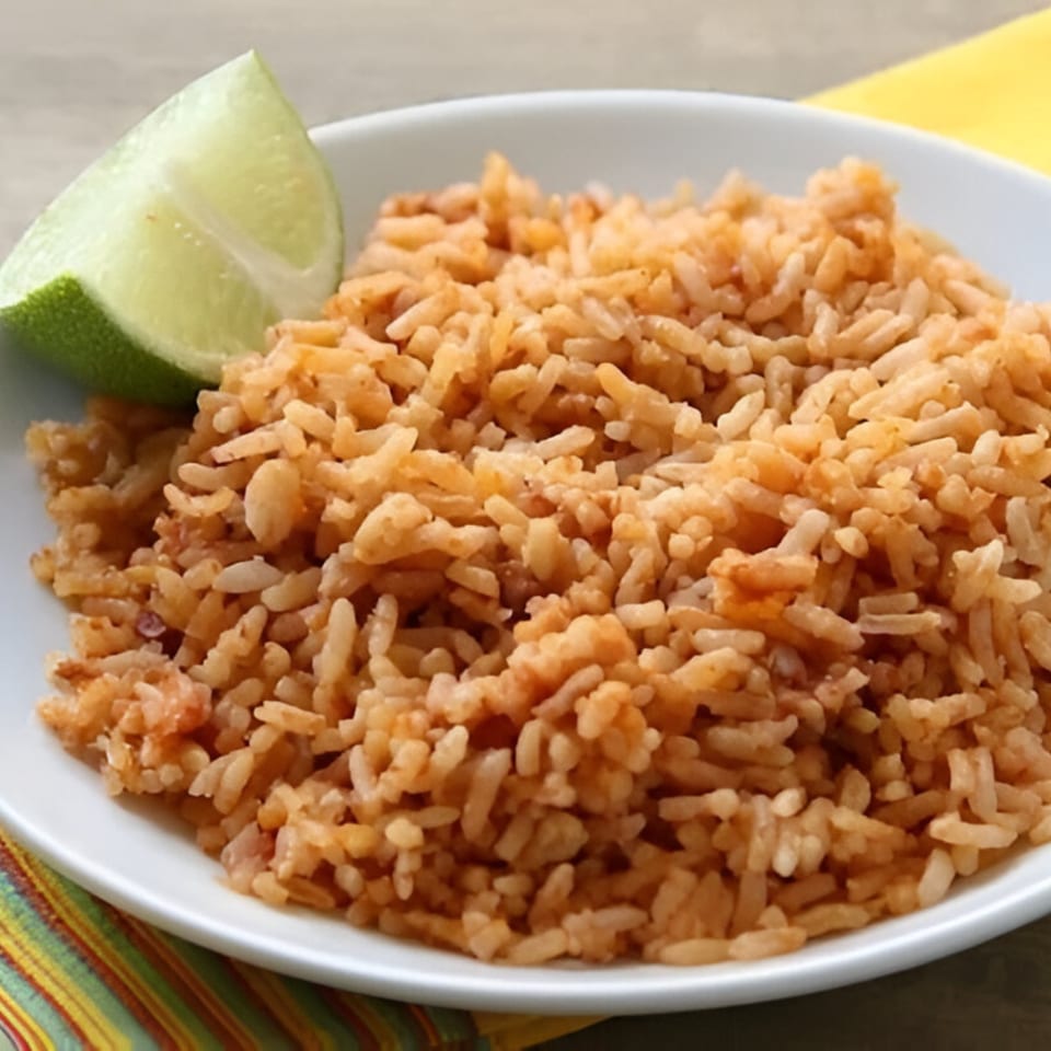 A white bowl filled with Mexican rice and a fresh lime wedge on a colorful striped placemat.