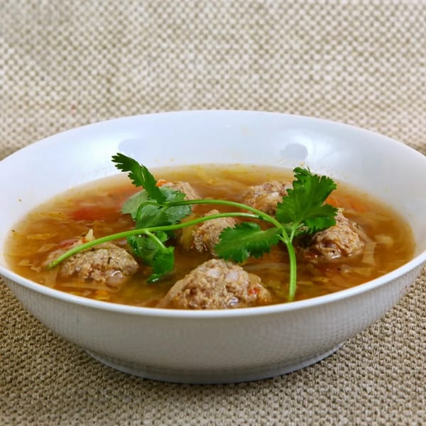 A white bowl of Mexican albondigas soup with meatballs, vegetables, and cilantro garnish.