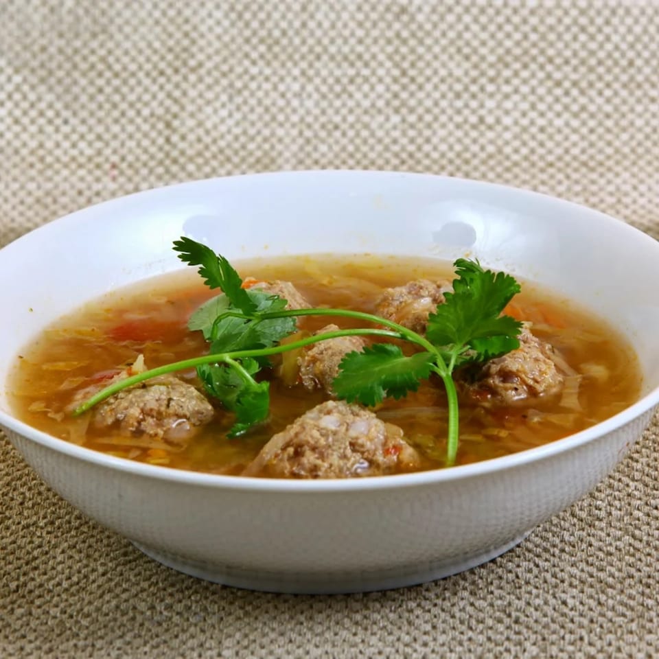 A white bowl of Mexican albondigas soup with meatballs, vegetables, and cilantro garnish.