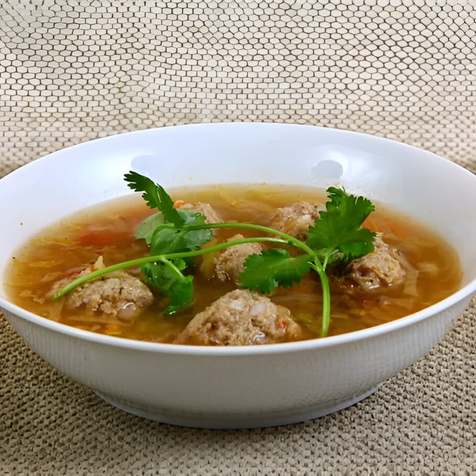 A white bowl of Mexican albondigas soup with meatballs, vegetables, and cilantro garnish.