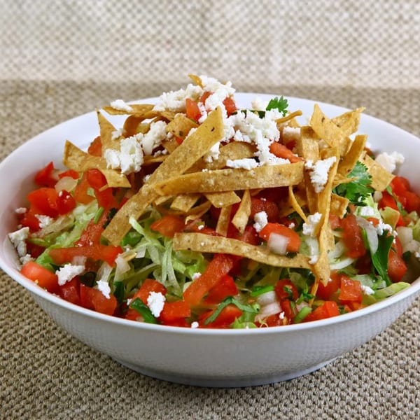 A vibrant Mexican salad with shredded lettuce, diced tomatoes, crumbled cheese, and tortilla strips.