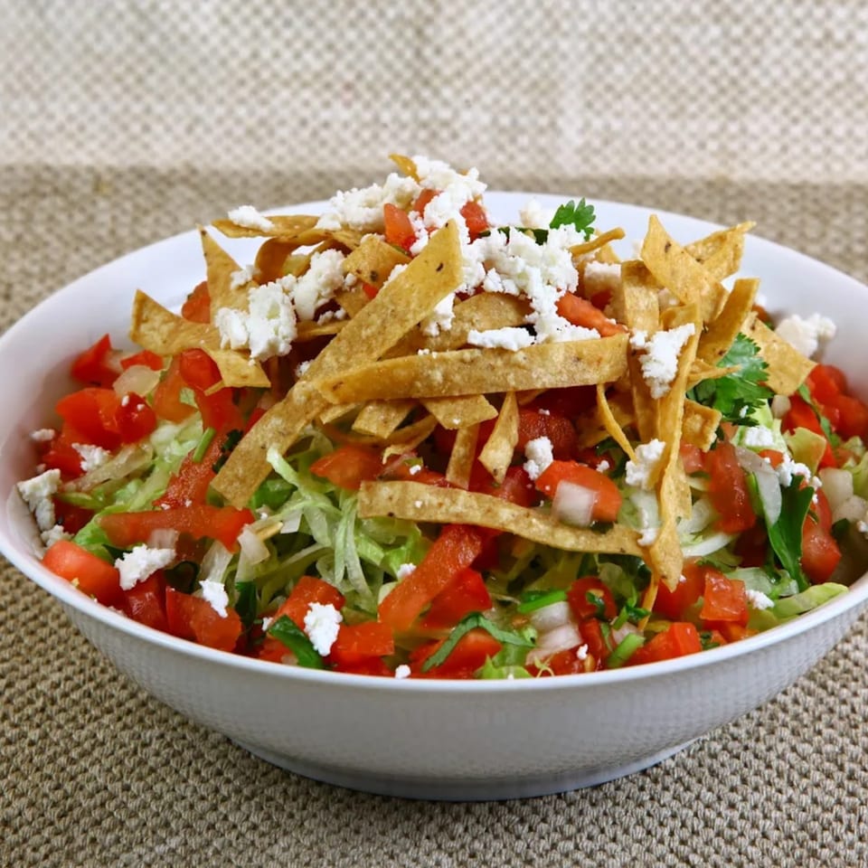 A vibrant Mexican salad with shredded lettuce, diced tomatoes, crumbled cheese, and tortilla strips.