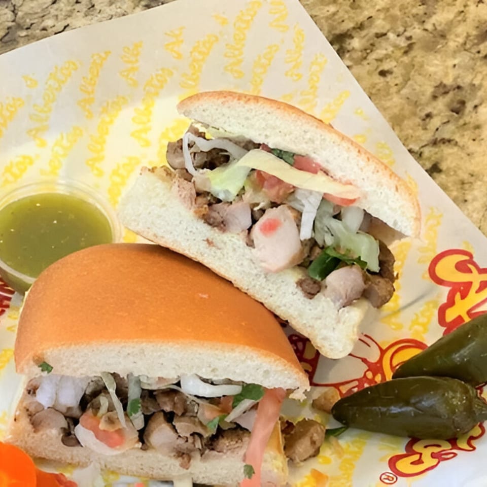 Two Alberto's Mexican tortas with meat, lettuce, tomato, onions, and a side of green salsa and jalapeños.